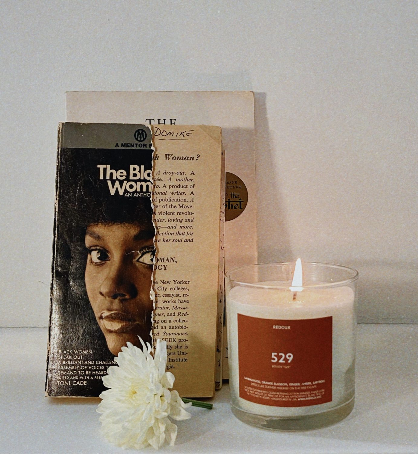 Redoux brand vegan skincare candle, styled next to book called the black woman because brand is a black owned brand